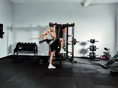 A Person exercising in a gym with a Altas Strength Smith machine and weights