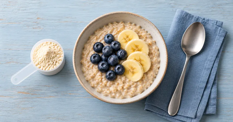 Oatmeal topped with blueberries and banana beside a scoop of protein powder on a pale blue breakfast table.